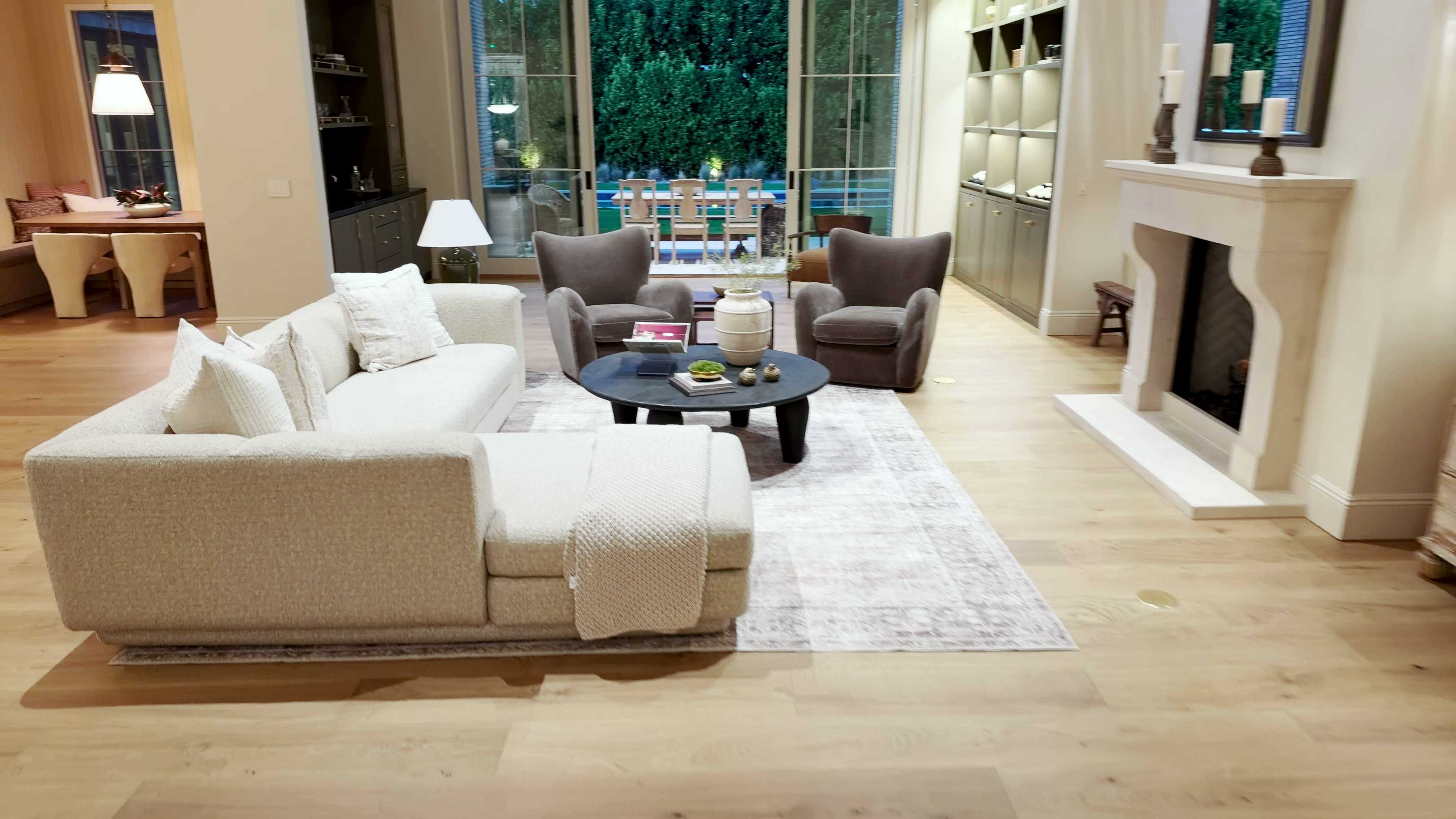 Living room with a white sectional sofa, a round coffee table, a stone fireplace and tall glass doors to the pool